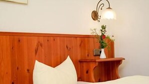 Een houten hoofdbord met een wit kussen en een klein tafeltje met een bloevas.