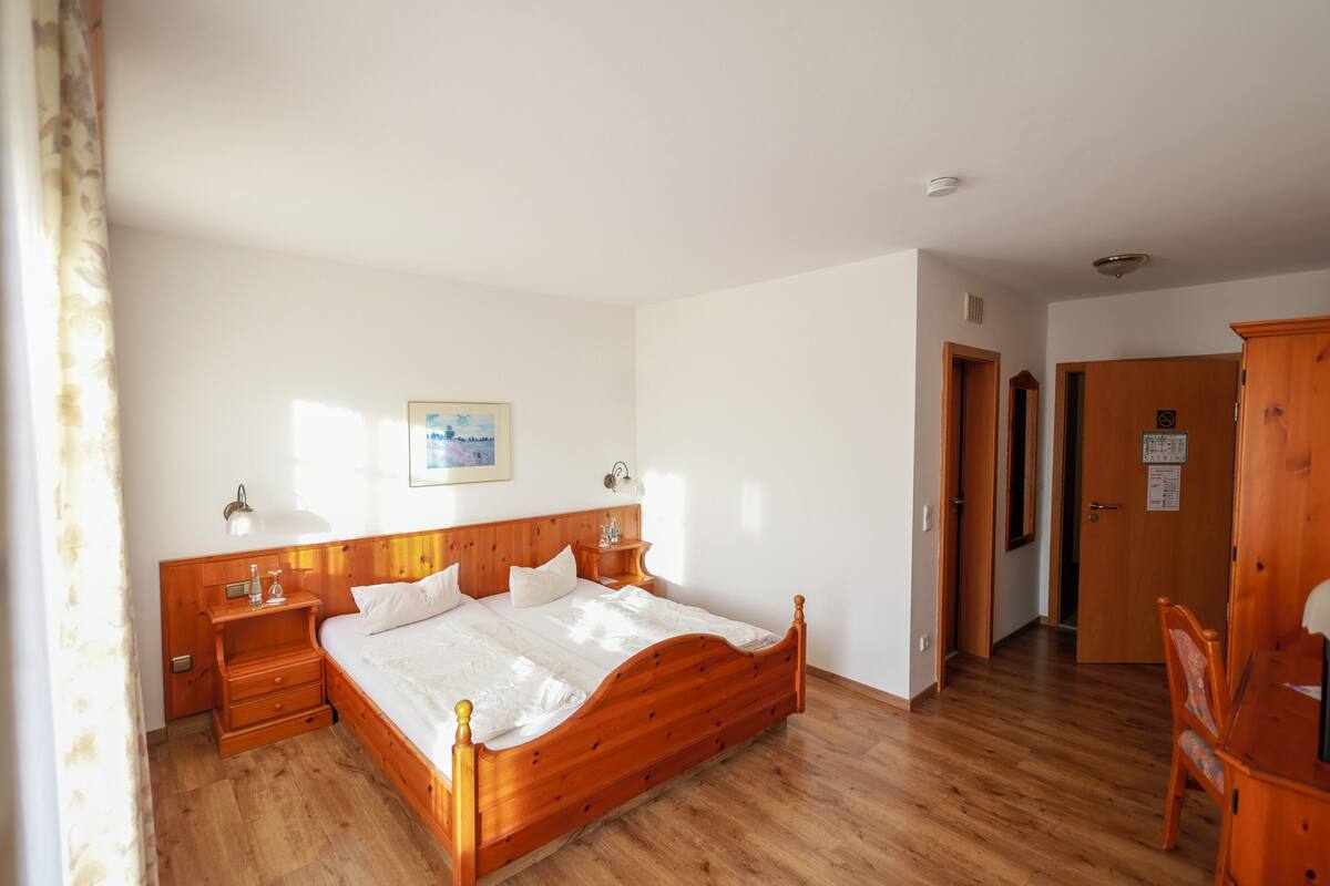 Une chambre à coucher avec un lit en bois, des tables de chevet, une commode, une armoire en bois et une porte donnant sur une autre pièce.