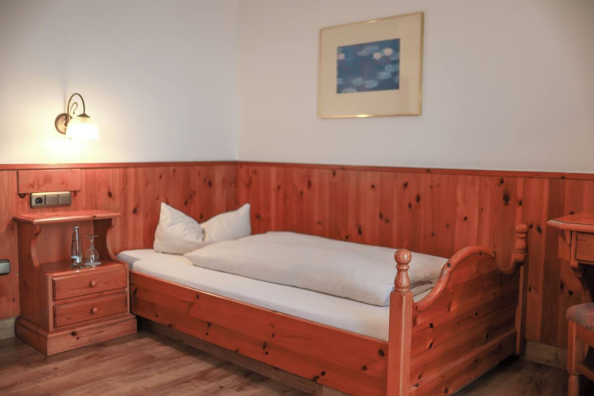 Un lit en bois avec un matelas et des oreillers blancs, une table de chevet avec une lampe et un tableau encadré au mur.