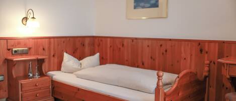 A wooden bed with a white mattress and pillows, a bedside table with a lamp, and a framed picture on the wall.