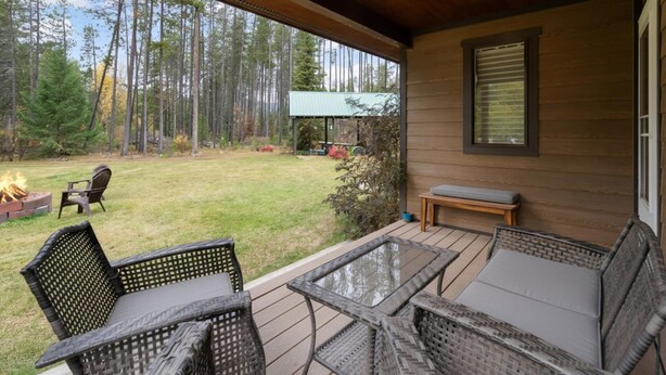 A covered patio with wicker furniture, a fire pit, and a view of a forest. - New listing! Cozy 2 bed cabin 10 mins to Glacier (Coram)