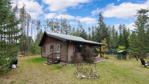 A cabin with a porch, surrounded by a grassy yard and tall trees. - New listing! Cozy 2 bed cabin 10 mins to Glacier (Coram)
