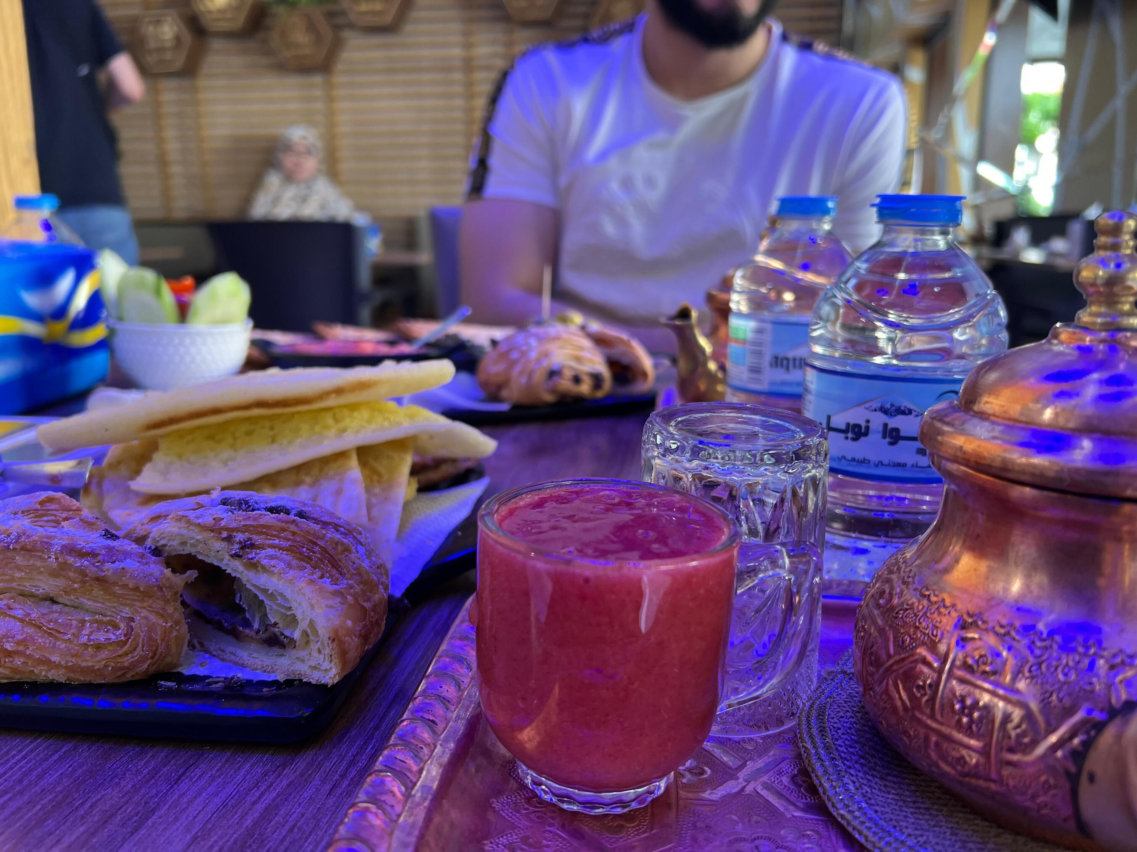 A dining table with food, a glass of red drink, and a copper pot.