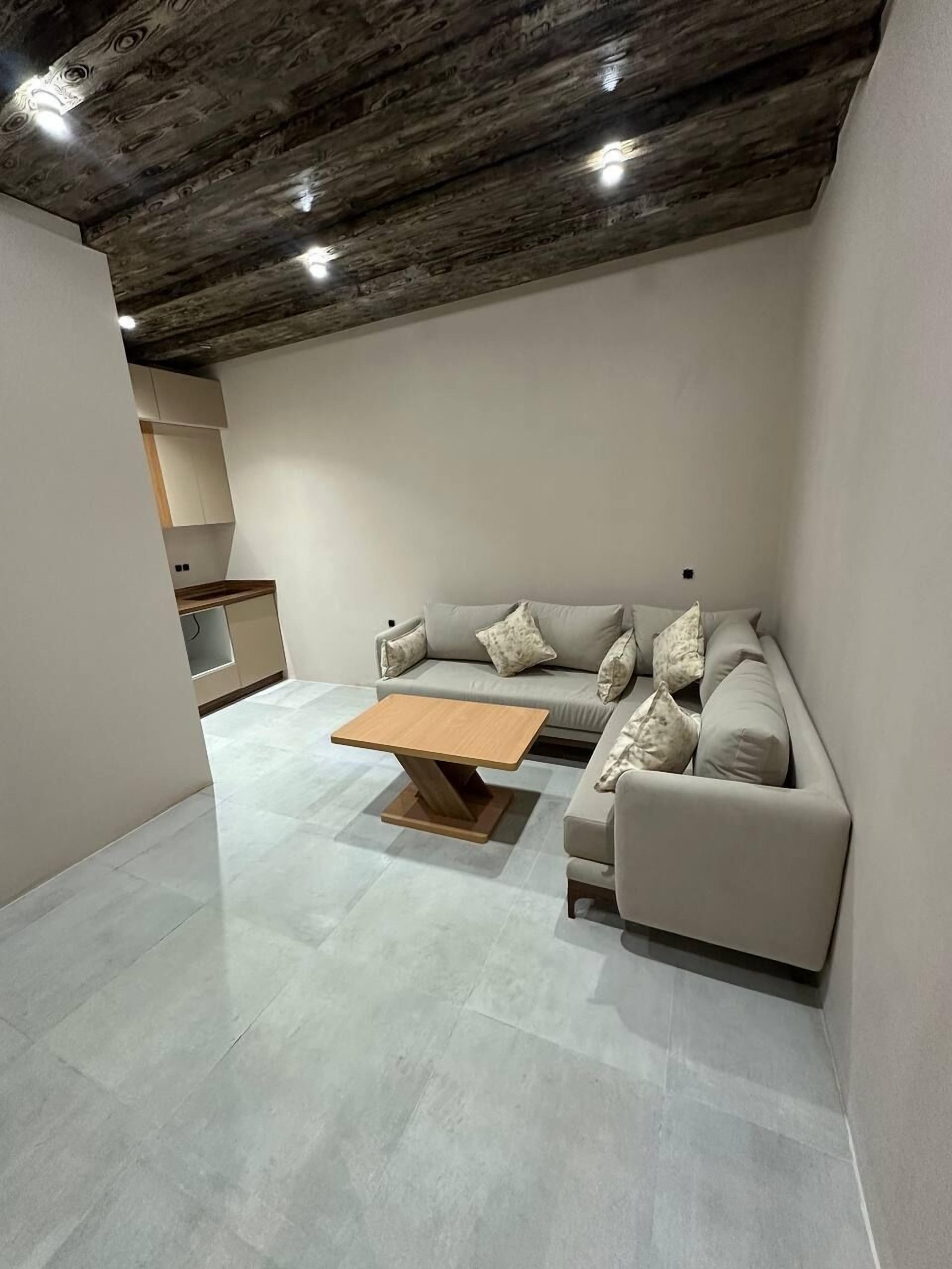 A modern living room with a sectional sofa, a wooden coffee table, and a kitchen area in the background.