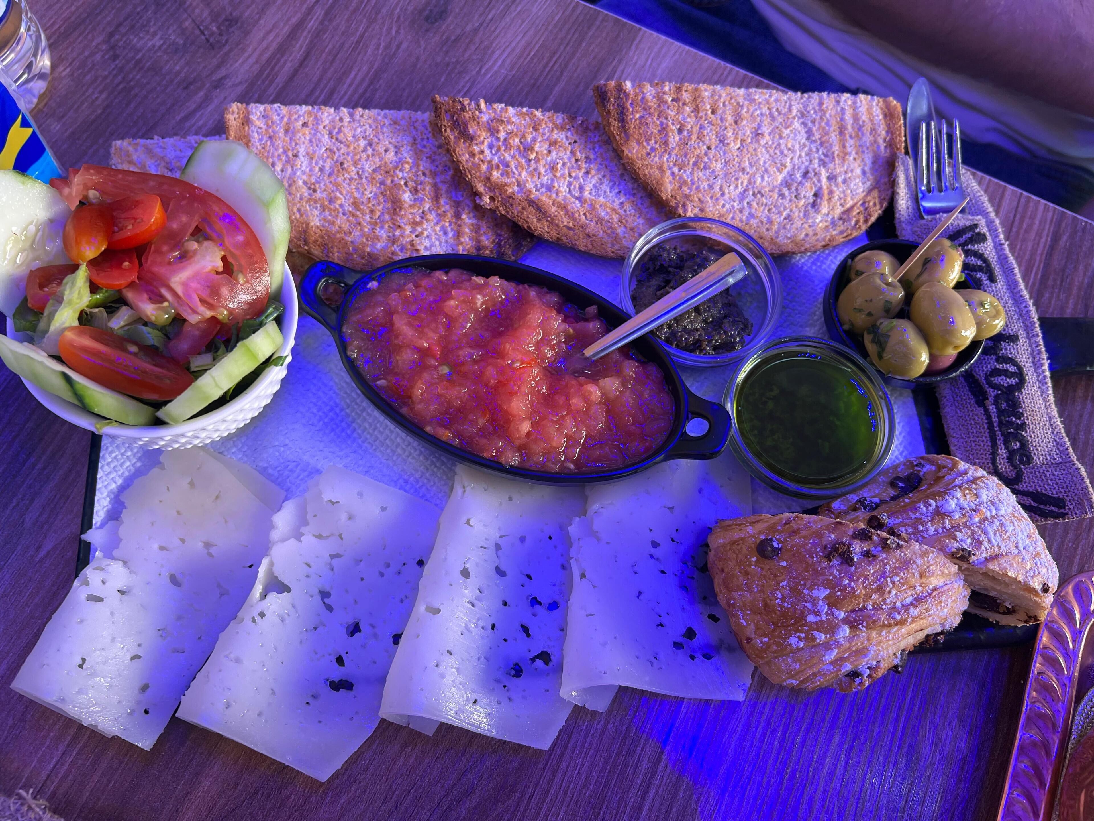 A meal with bread, salad, and a bowl of tomato-based dish on a wooden table.