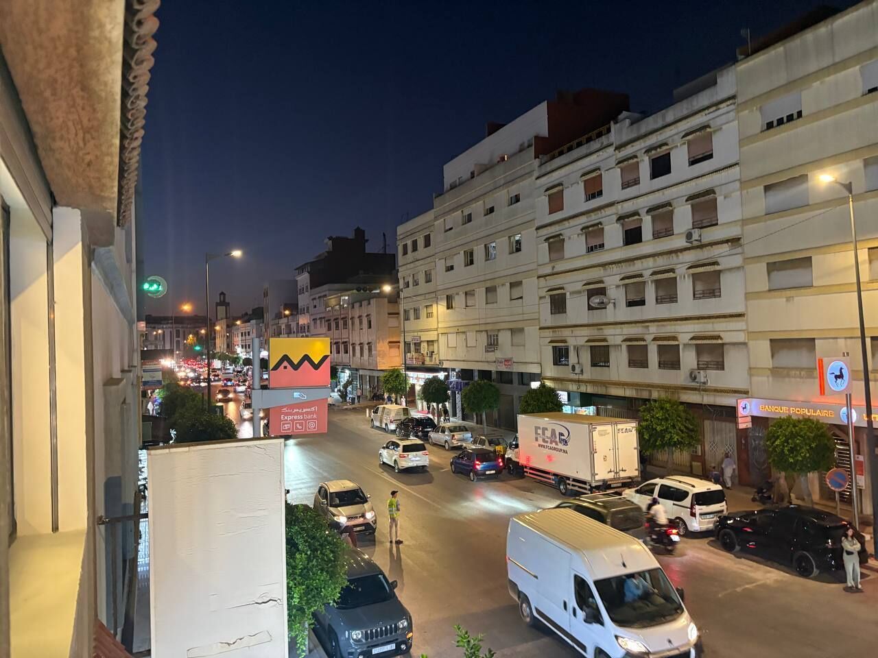 A busy urban street at night with buildings, vehicles, and illuminated signs.