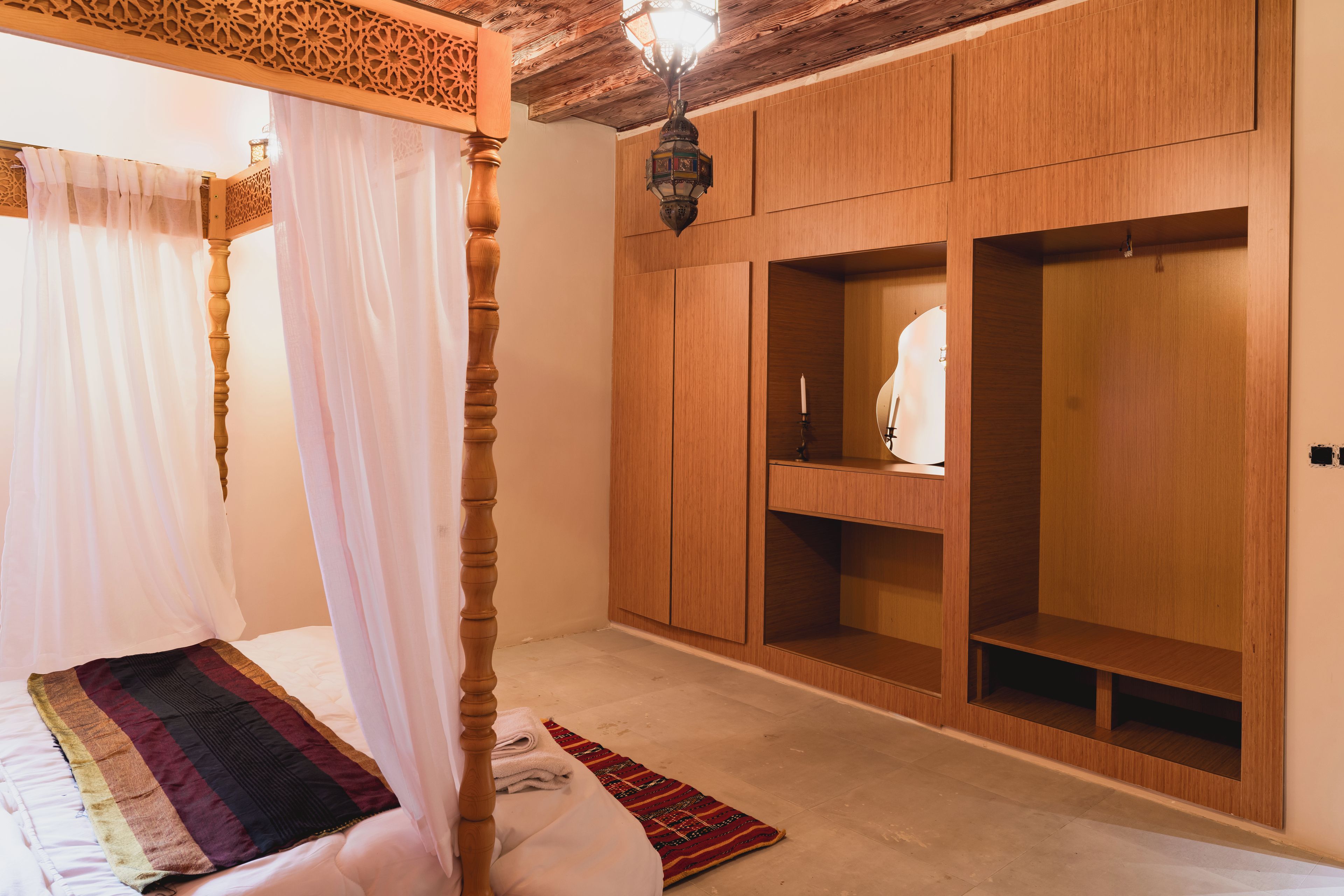 A bedroom with a four-poster bed, wooden wardrobe, and a hanging lamp.