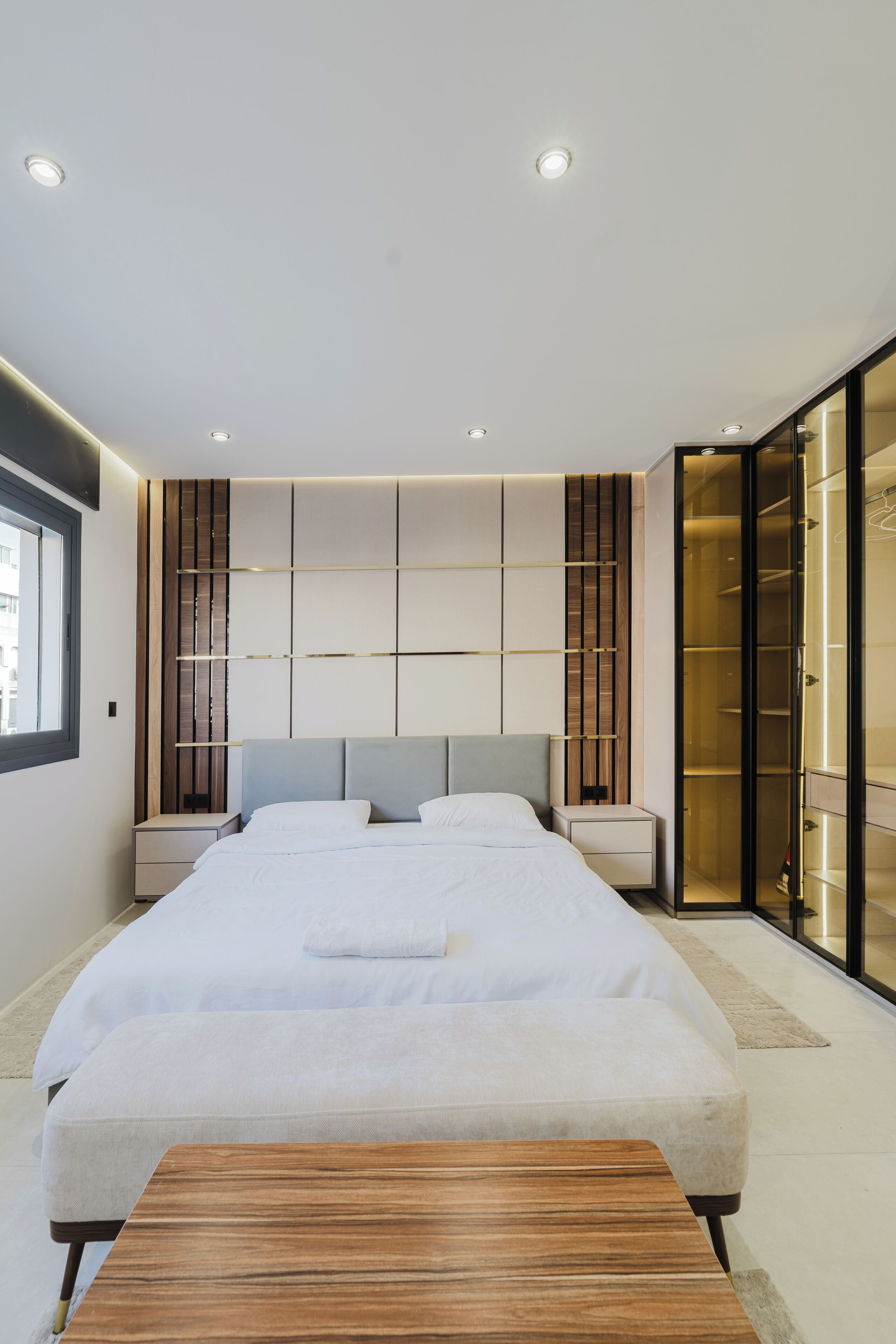 Une chambre moderne avec un grand lit, des tables de chevet, un banc en bois et un dressing.