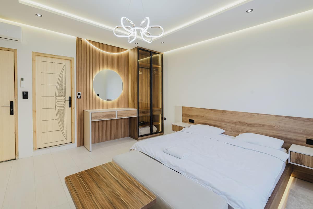 A modern bedroom with a large bed, a vanity with a mirror, and a wooden wardrobe.