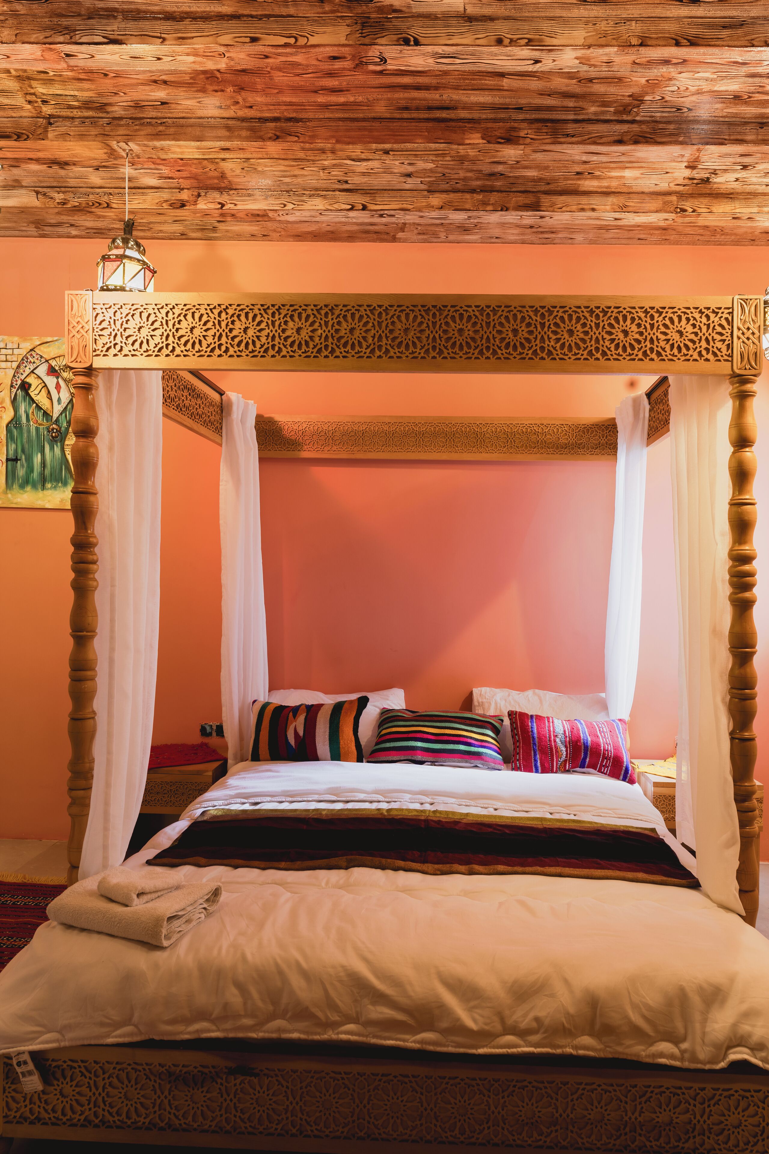 A four-poster bed with a canopy, a wooden ceiling, and a painting on the wall.