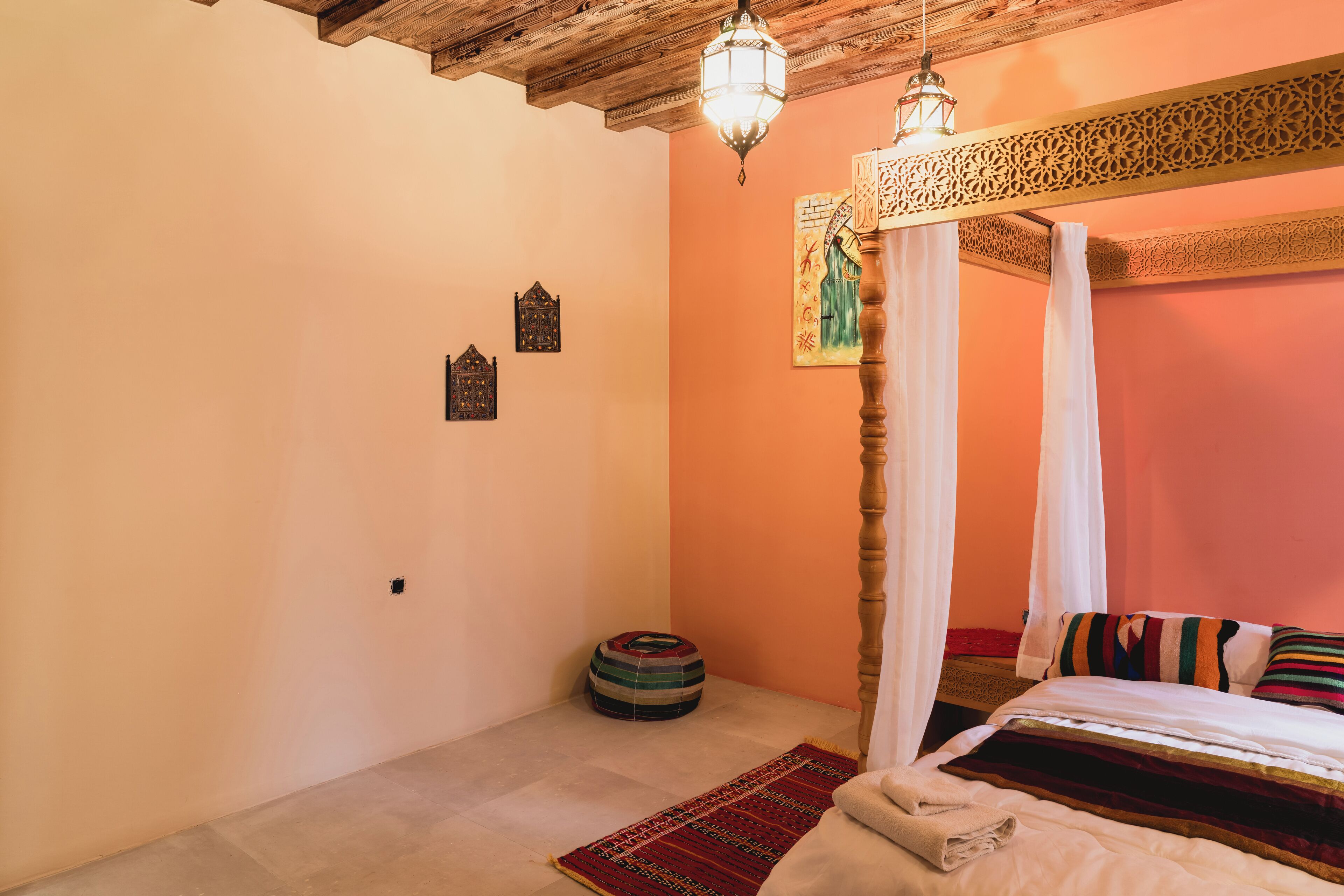 A bedroom with a four-poster bed, a hanging lantern, a patterned rug, and a small decorative item on the floor.
