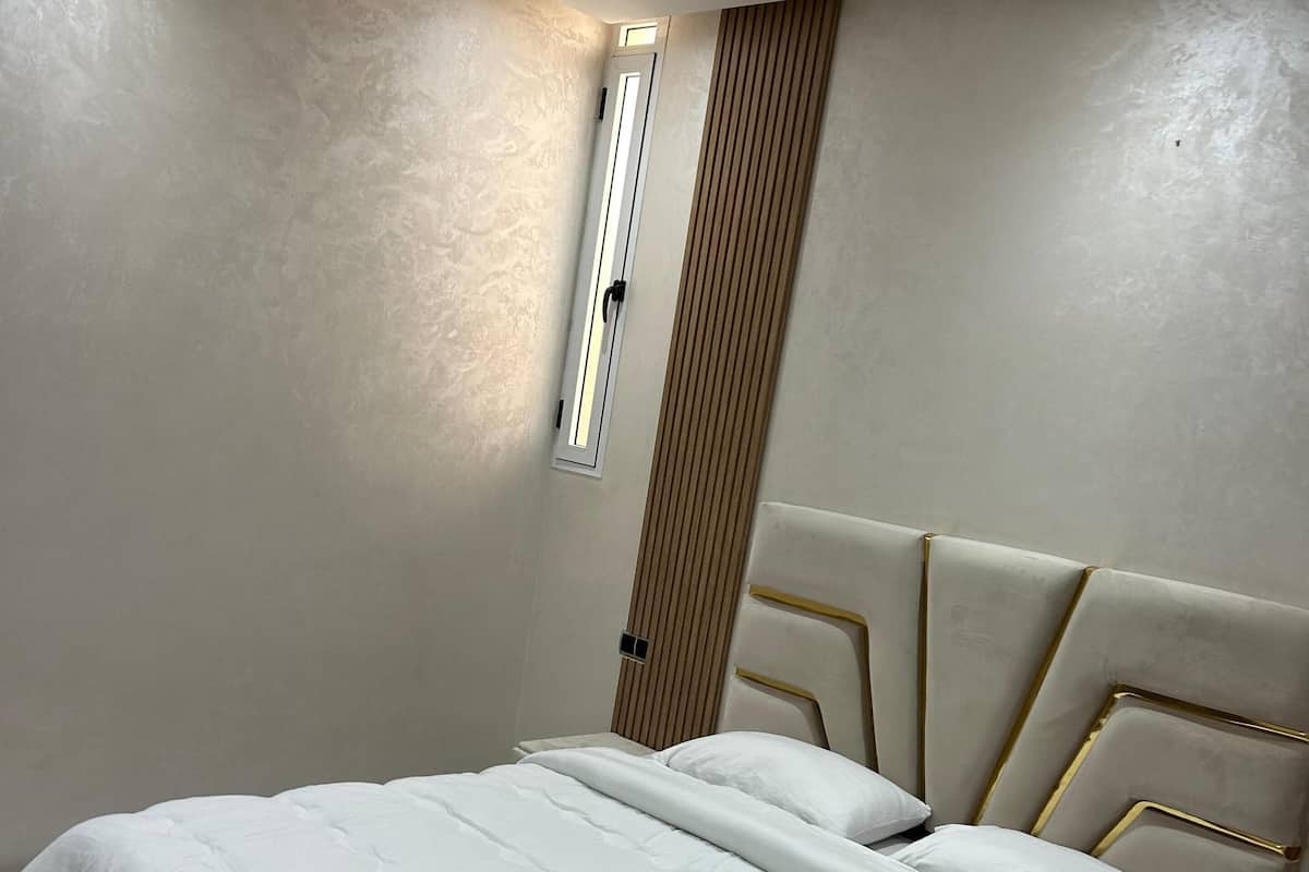 A neatly made bed with white linens and a folded towel, a bedside table with a drawer, and a wall-mounted light fixture.