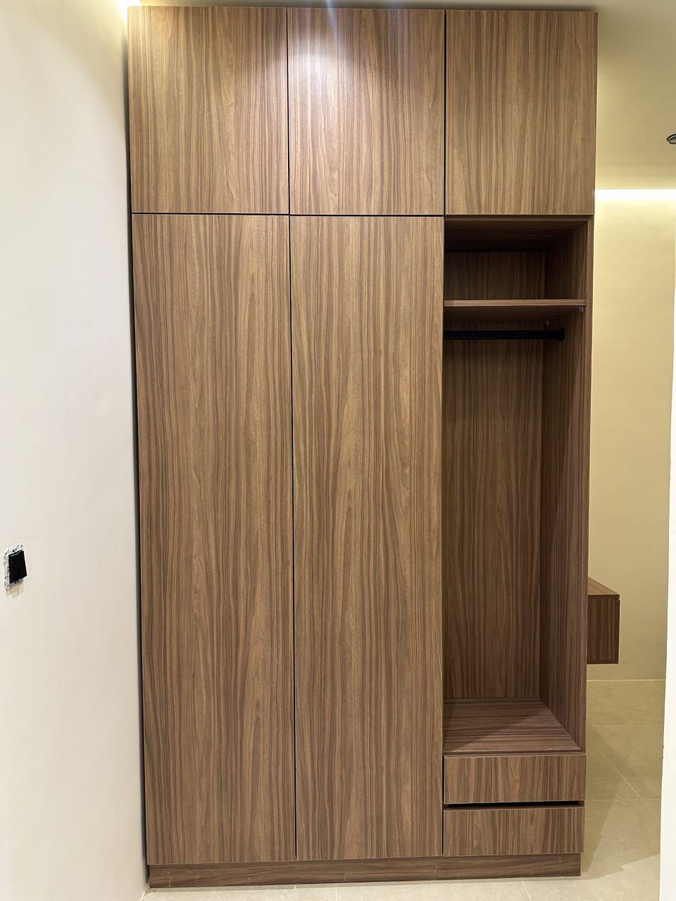 A wooden wardrobe with multiple compartments and a hanging rod.