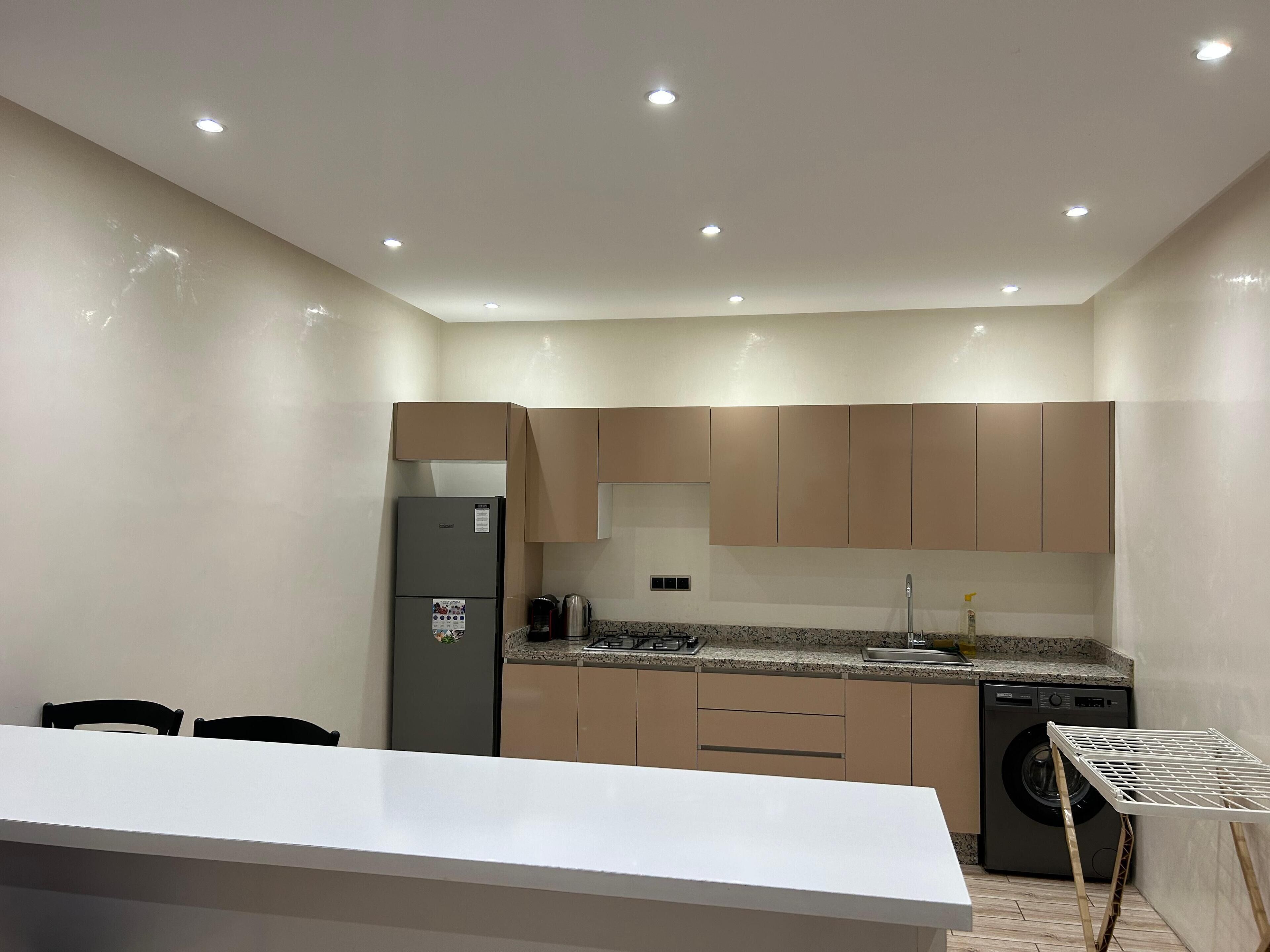 Una cocina moderna con encimera blanca, armarios color beige, lavavajillas empotrado y pileta de acero inoxidable.