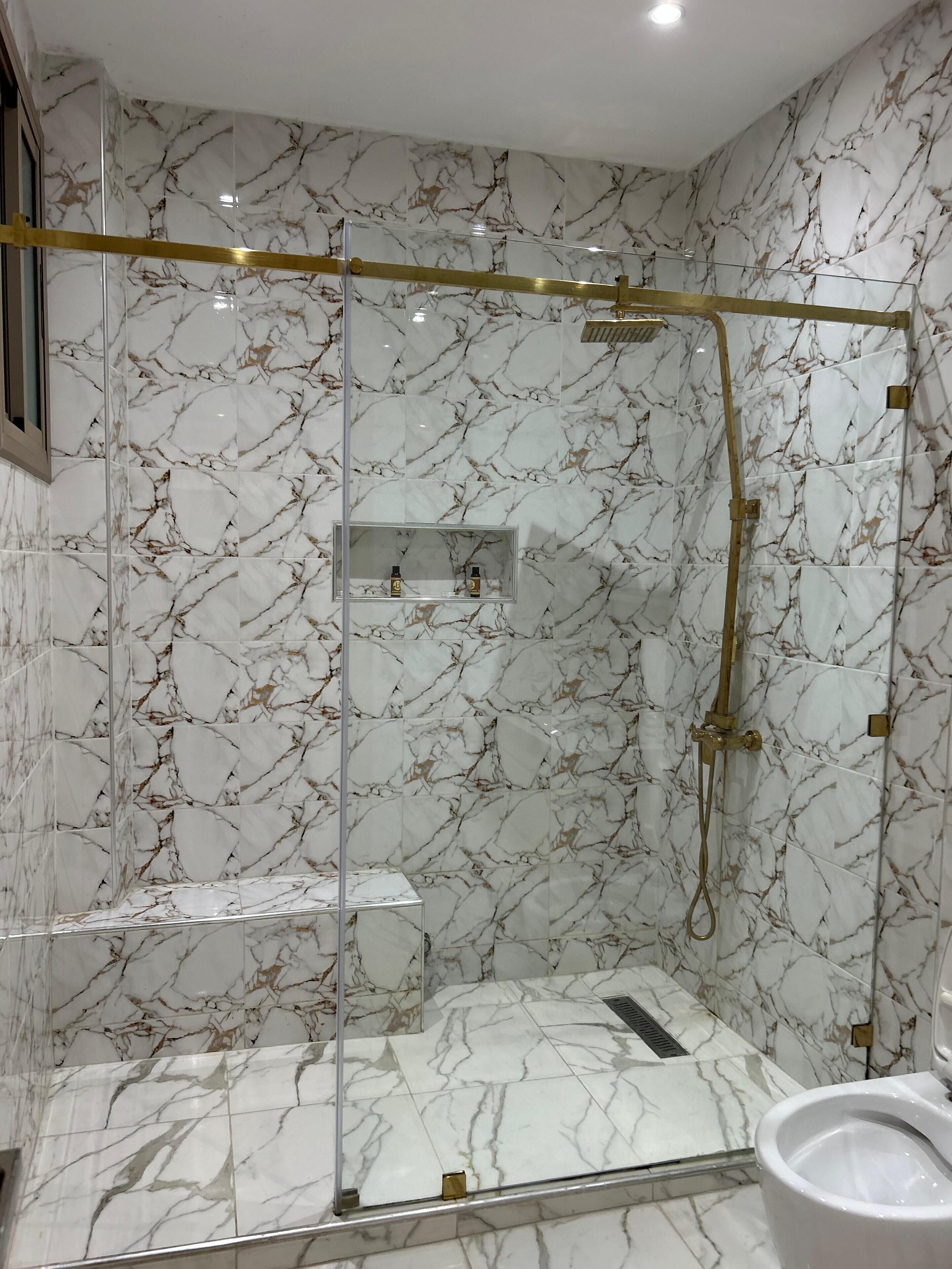 A modern bathroom with marble walls and a glass-enclosed shower area.