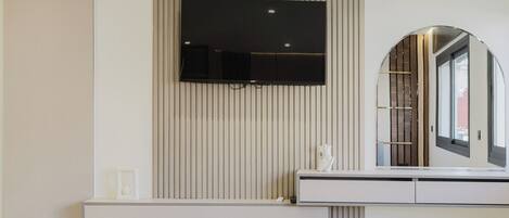 Une chambre à coucher moderne avec un téléviseur fixé au mur, une table de chevet et un grand miroir.