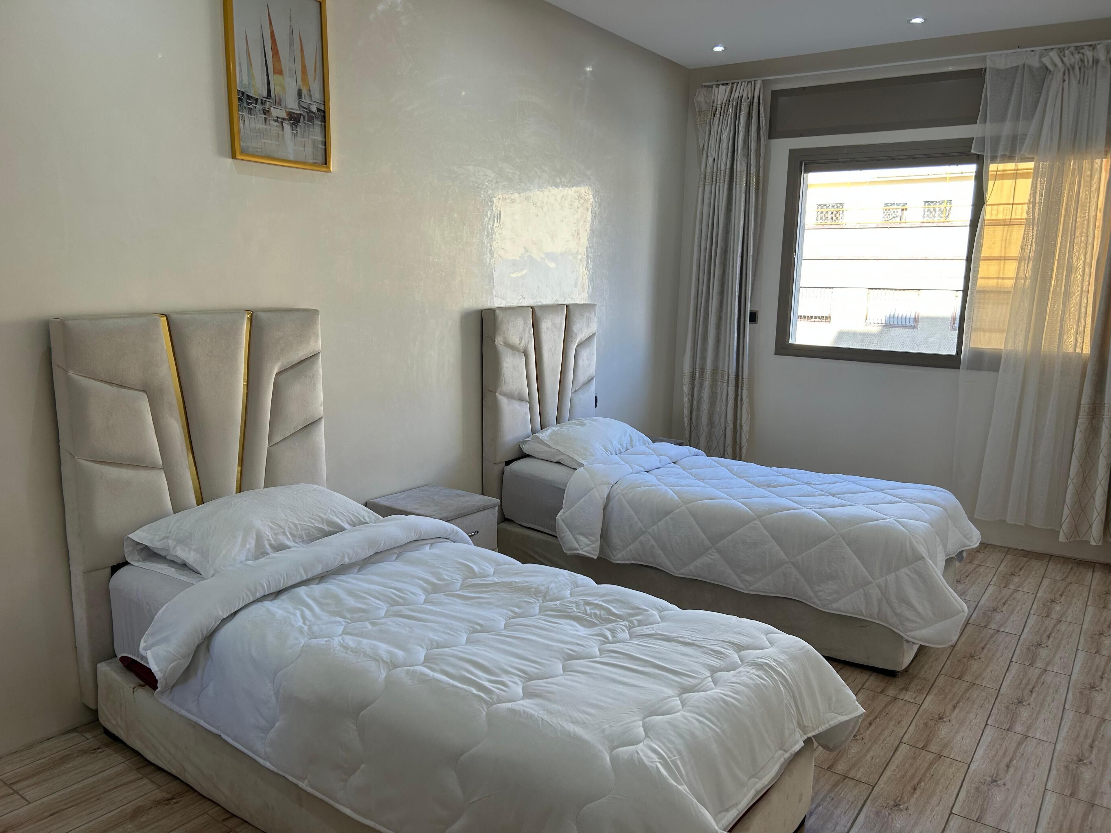 Ein Hotelzimmer mit zwei Betten, einem Bild an der Wand und einem Fenster mit Vorhängen.