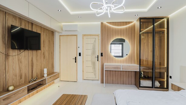 A modern bedroom with a TV mounted on a wooden panel wall, a bedside table, a bed with white bedding, and a walk-in closet with a mirror. - el boujdaini (Tangier)