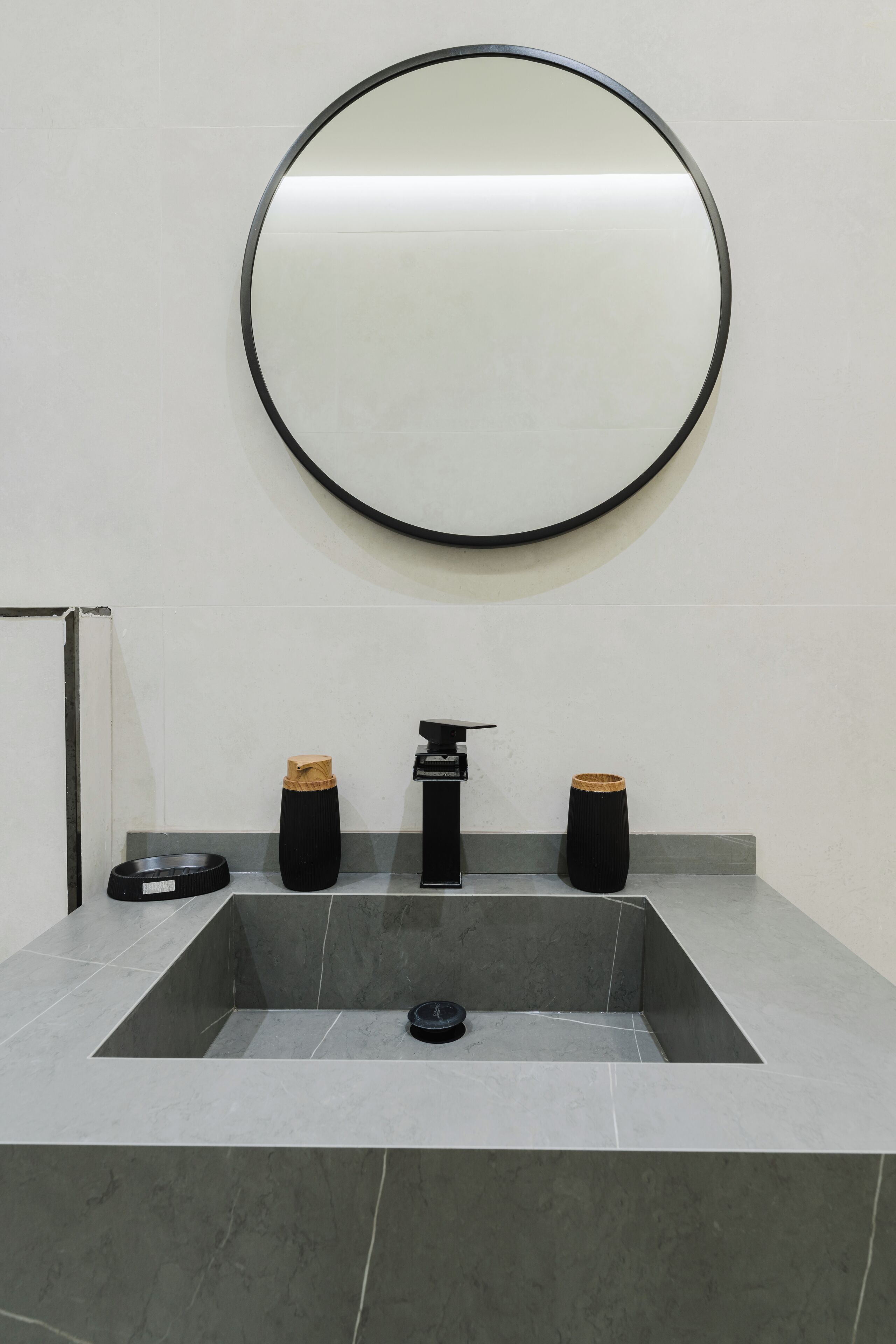 A bathroom with a rectangular sink, a round mirror, and two black vases on the counter.