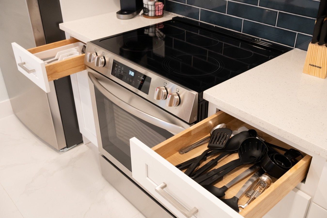 A kitchen with a stainless steel oven, a black induction cooktop, and a drawer with kitchen utensils.