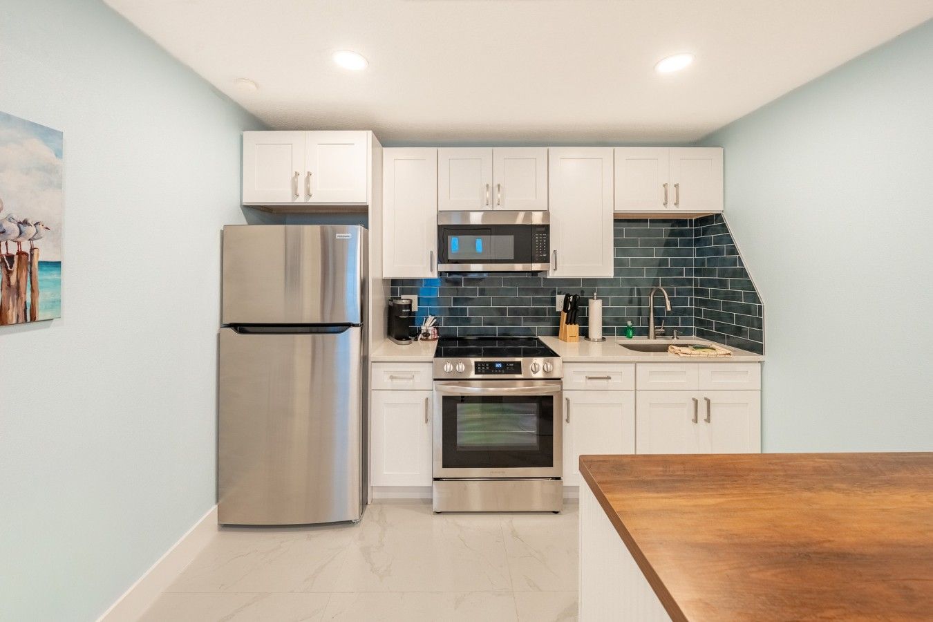 Una cocina compacta con armarios blancos, electrodomésticos de acero inoxidable y un salpicadero de azulejos azules.