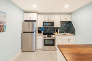 A compact kitchen with white cabinets, stainless steel appliances, and a blue-tiled backsplash. - Clearwater Bliss Apartments 2 (Clearwater)