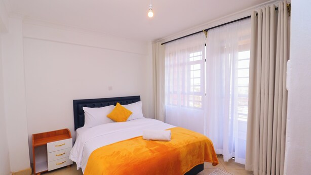 A neatly arranged bedroom with a bed, a bedside table, and curtains. - Serene Homes Membley- Executive 1-Bedroom in Ruiru- Secure & Affordable (Ruiru)