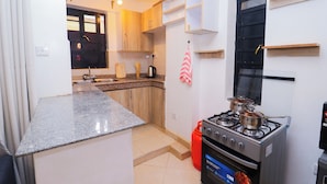 A compact kitchen with granite countertops, wooden cabinets, a gas stove, and a small window. - Serene Homes Membley- Executive 1-Bedroom in Ruiru- Secure & Affordable (Ruiru)
