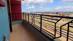 A balcony with a metal railing overlooking a street with buildings and vehicles. - Serene Homes Membley- Executive 1-Bedroom in Ruiru- Secure & Affordable (Ruiru)