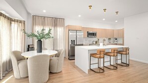 Een moderne keuken met een centraal eiland, roestvrijstalen apparatuur en een eethoek met een ronde tafel en stoelen.