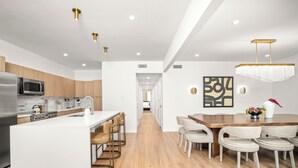 Een moderne keuken met een centraal eiland, roestvrijstalen apparatuur en een eethoek met een houten tafel en stoelen.