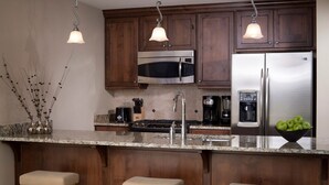 A kitchen with dark wooden cabinets, stainless steel appliances, a granite countertop, and pendant lighting. - New Sunrise Gondola at Ski-in/out Condo Sunrise Lodge in Canyons Village Jan 03 (Park City)