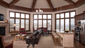 A spacious living room with a fireplace, a large sofa, and a dining area with a view through large windows. - New Sunrise Gondola at Ski-in/out Condo Sunrise Lodge in Canyons Village Jan 03 (Park City)