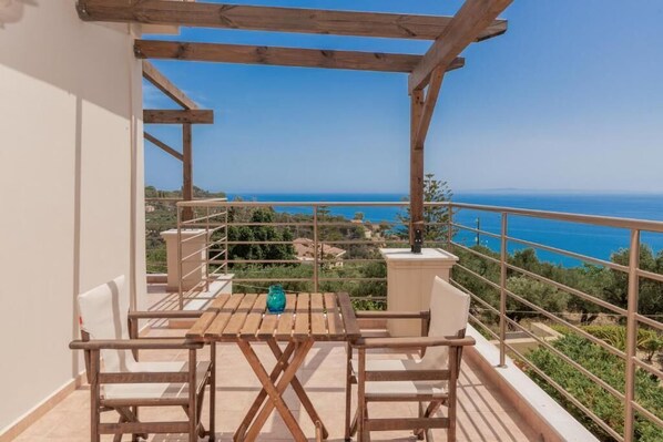 Eine Hollaube mit Tisch und Stühlen auf einem Balkon mit Blick auf die Küste.