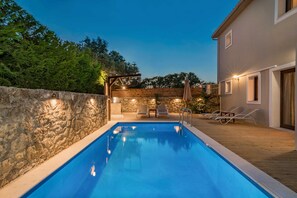 Ein Schwimmbad mit Holzterrasse, Steinmauer und Liegestühlen.