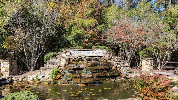Un étang avec une cascade, entouré de murs de pierre et d’arbres aux feuilles d’automne.