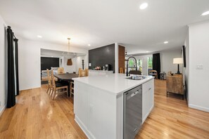 Een moderne keuken met een centraal kookeiland, houten vloeren en inbouwspots.