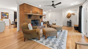 Un salon avec une cheminée en briques, deux canapés, un ventilateur de plafond et un coin repas avec une table et des chaises.