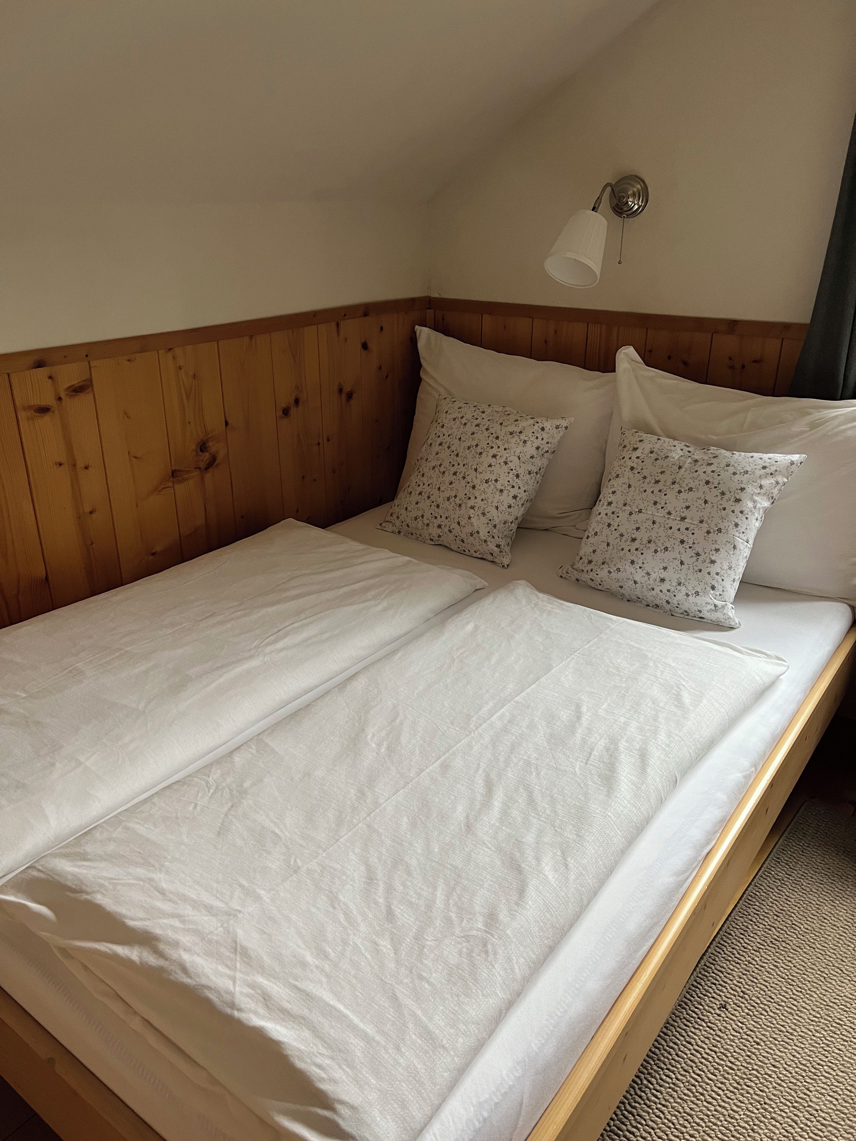 Una cama individual con cabecera de madera, dos almohadas y una lámpara fijada a la pared.