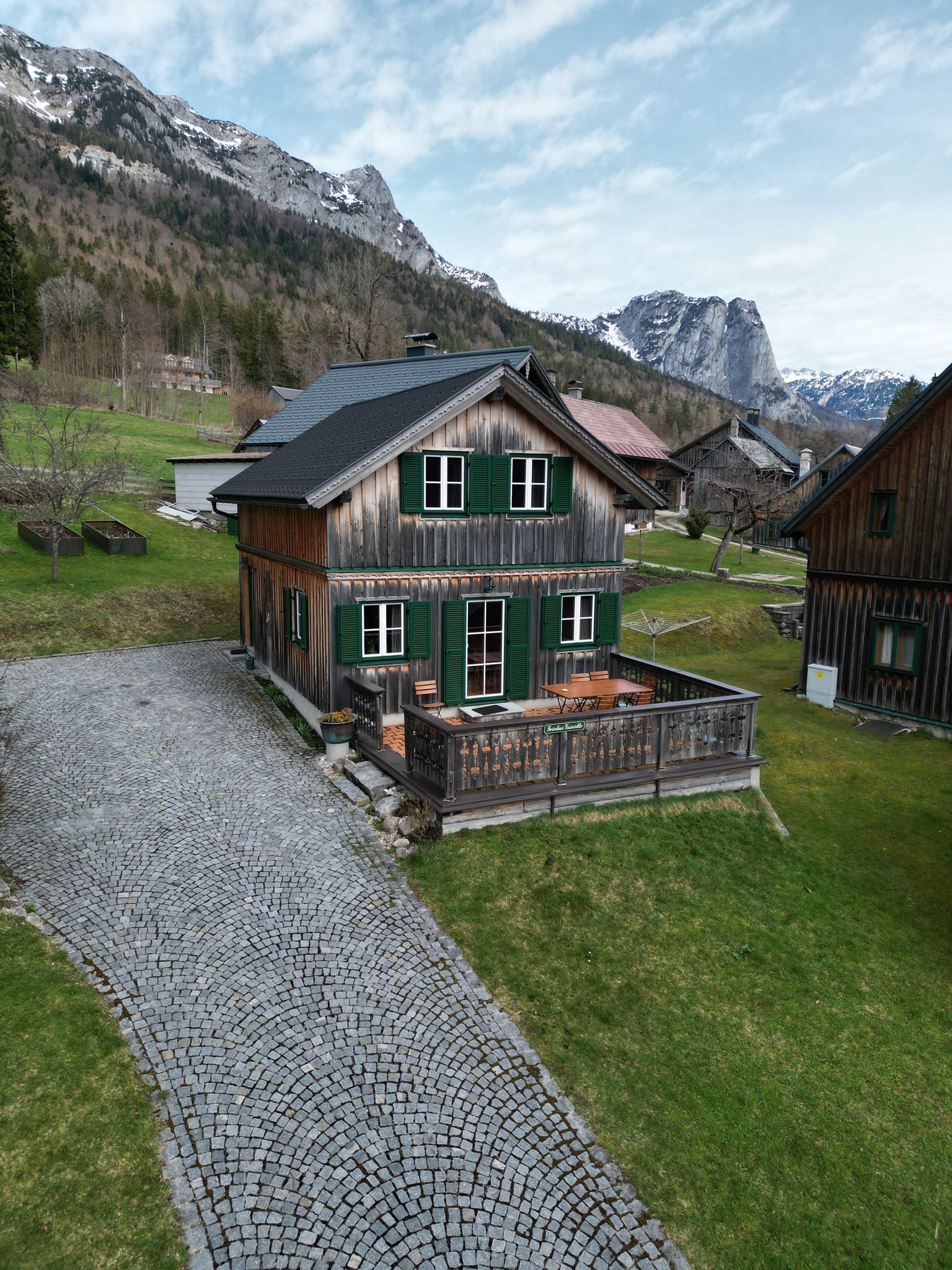 A wooden house with a paved driveway and a mountain backdrop.