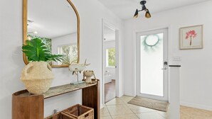 Un couloir avec un grand miroir, une plante, des paniers en osier et une porte donnant sur une autre pièce.