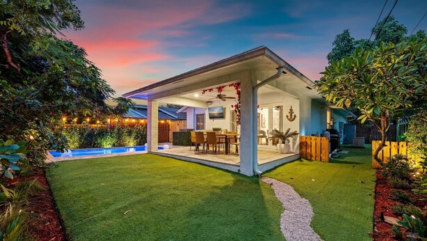 Une maison moderne dotée d’un patio couvert, d’une piscine et d’une végétation luxuriante.