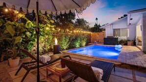 Un jardin avec une piscine, des meubles d’extérieur, des guirlandes lumineuses et un foyer.