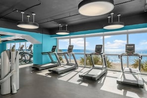 A gym with treadmills and exercise equipment, large windows with a beach view, and a modern ceiling design.