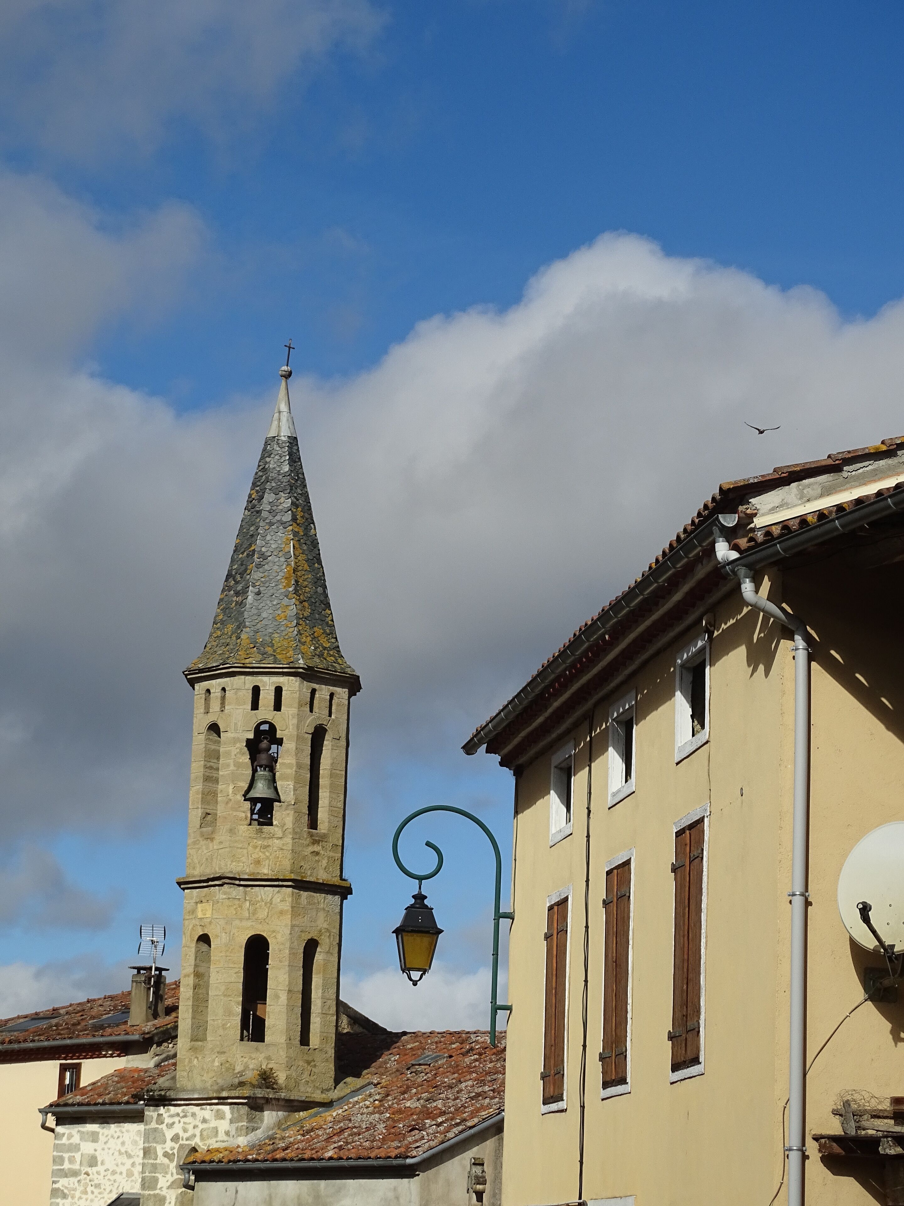 Una torre histórica con campana, farol y edificios tradicionales con contraventanas de madera.