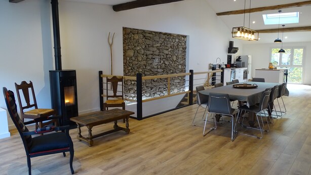 A spacious living area with a stone wall, a fireplace, and a dining table with chairs. - Country house in the Ariege ideal for skiing, hiking, biking, snowshoeing, fishing... (Gudas)