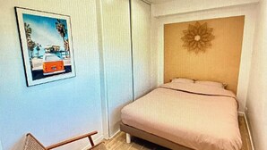 Quarto com cama, cadeira, quadro na parede e janela com cortinas.