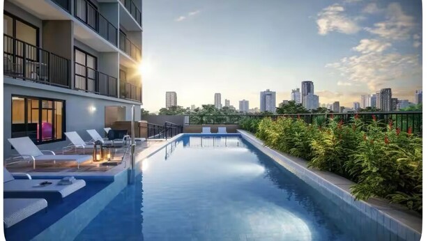 Une piscine sur le toit, agrémentée de chaises longues, avec une vue sur les toits de la ville en arrière-plan et un immeuble doté de balcons.