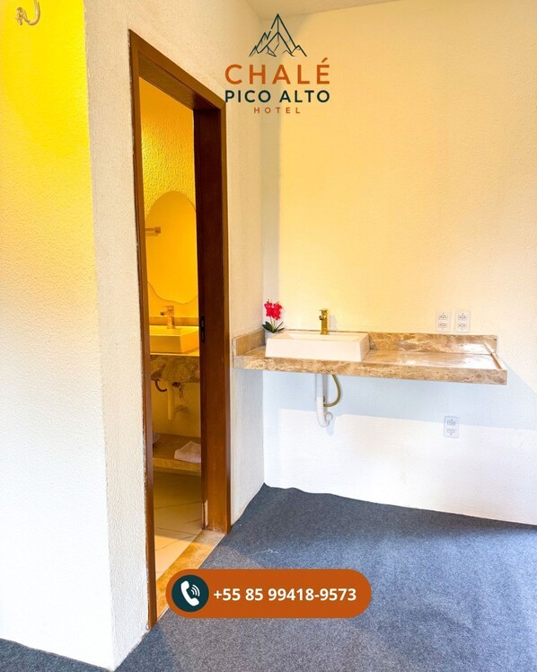 Baño de hotel con lavamanos, espejo y una puerta que da a otra habitación.