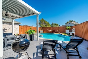 Un patio trasero con piscina, mobiliario exterior y una parrilla.